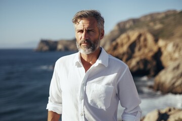 Portrait of a glad man in his 50s wearing a classic white shirt isolated in rocky shoreline background