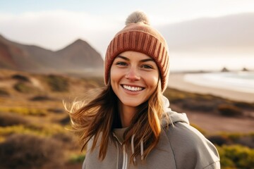 Portrait of a smiling woman in her 30s sporting a trendy beanie isolated in serene dune landscape background