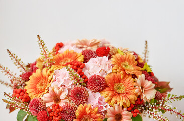 Autumn bouquet in warm colors. Red, yellow, orange, pink flowers and dry leaves. Floral arrangement on a white background. Autumn background for Thanksgiving and other fall holidays card design.