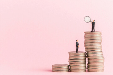 Miniature figures analyzing financial growth atop stacked coins, pink background.