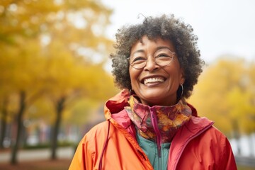 Wall Mural - Portrait of a joyful afro-american woman in her 70s wearing a lightweight packable anorak while standing against bright and cheerful park background