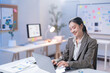 © Tj - Young asian businesswoman works late in the office, focused on her laptop with a smile, showing determination and confidence in a modern setting