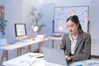 © Tj - Asian businesswoman is working late in her office, focused on her laptop and surrounded by paperwork and digital devices