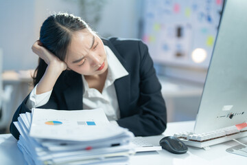 Exhausted businesswoman overwhelmed by heavy workload at office desk, surrounded by paperwork and laptop, showing signs of burnout and stress