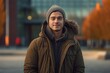 © Markus Schröder - Portrait of a satisfied man in his 20s wearing a warm parka while standing against modern university campus background