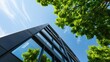 © Shutter2U - Low angle view of a modern office building with trees and a blue sky.