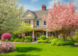 © ProArt Studios - Beautiful exterior home with green grass yard, trees in bloom, and flowering bushes during morning spring time.