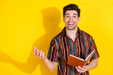 Wall Mural - Portrait of nice young man talk hold book wear shirt isolated on yellow color background