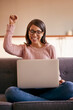 © peopleimages.com - Excited, celebration and woman with laptop, win and cheering for victory, home and online competition. Notification, happy and person with joy, lottery and success in living room, fist and house