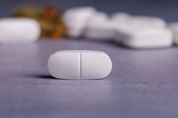 Detailed view of a white pill on a concrete table, contrasted with a colorful collection of pills in the background, emphasizing diversity