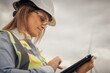 © YURIMA - At a busy construction site, a skilled female worker uses a tablet to communicate and collaborate with her team, enhancing efficiency and productivity in various tasks and operations