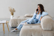 © F8  \ Suport Ukraine - Happy beautiful woman is talking on a phone sitting on a sofa at home.