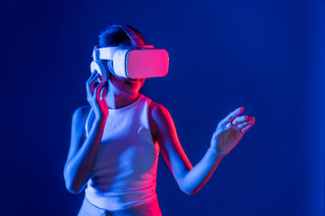 Smart female standing with surrounded by cyberpunk neon light wear VR headset connecting metaverse, futuristic cyberspace community technology. Woman using hand touching virtual object. Hallucination.