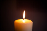 A single candle flame illuminating darkness in a serene indoor setting during evening hours. Baccground for funeral, obituary, in memoriam with copy space