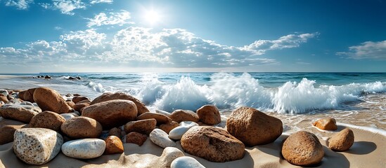 Wall Mural - Rocks scattered along the edge of a sandy beach with waves crashing gently against them under a bright sky