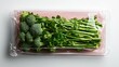 ©  Shomixer - A bundle of fresh broccoli is enclosed in clear wrap against a pink background, showcasing freshness and the health benefits of green vegetables.