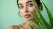 © schiers_images - A beautiful woman with clear skin poses alongside a fresh aloe vera plant, emphasizing natural beauty and skincare. The green background enhances the overall feeling of freshness and vitality.