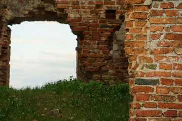 A window without glass in the ruined wall of an old building. The remains of an old red brick church or castle.