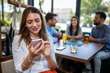 Woman using her phone in the restaurant. Her friends are in the background.