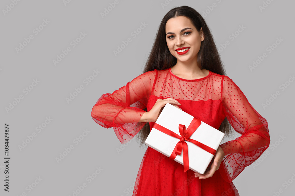 Beautiful young woman with Christmas gift on grey background