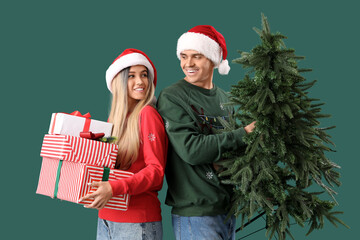 Canvas Print - Young couple in Santa hats with Christmas tree and gifts on green background