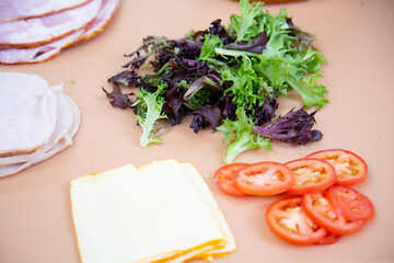 ingredients for a deli sandwich; meat, cheese, lettuce, and tomatoes