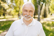 © dikushin - Over shoulder portrait of handsome gray-haired senior man standing posing in sunshine at summer park, smiling looking at camera on background of beauty nature, reflecting vibrant retirement lifestyle.