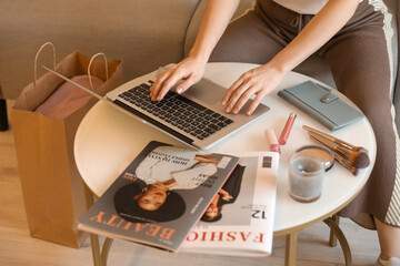 Wall Mural - Woman with laptop and makeup products shopping online on table at home, closeup