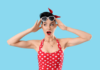 Wall Mural - Surprised young pin-up woman in sunglasses on blue background