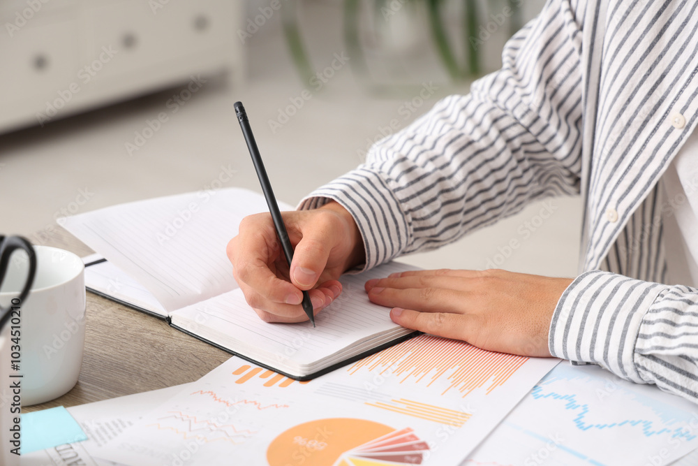 Male economist writing on notebook at table in office, closeup