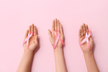 Wall Mural - Female hands with awareness ribbons on pink background, closeup. Breast cancer concept