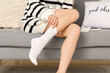 © Pixel-Shot - Woman putting white socks on sofa at home, closeup