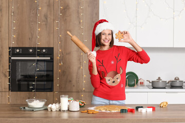 Wall Mural - Young woman with rolling pin making gingerbread cookies in kitchen on Christmas eve