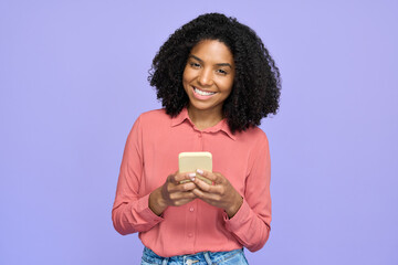 Wall Mural - Young happy African gen z model student wearing pink shirt standing isolated on purple background looking at camera holding smartphone. Smiling Afro American woman using mobile phone advertising apps.