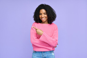 Wall Mural - Happy young African girl model pointing at copy space isolated on purple background. Smiling Afro American female customer looking at camera advertising promo, presenting ads shopping offer.