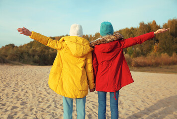 Back view happy joyful two women friends on sunny beach, stylish girlfriends together on sea coast