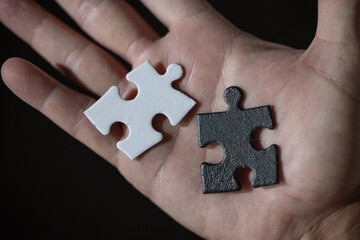 A hand holding two puzzle pieces, one white and one black both pieces have the same shape. The choice is a difficult concept.