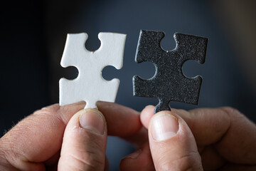 A hand holding two puzzle pieces, one white and one black both pieces have the same shape. The choice is a difficult concept.