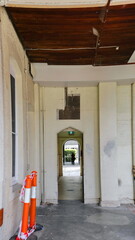 An entrance leads to a space in an abandoned mansion with two striking orange poles on the left. The white walls contrast with the decaying surroundings, giving the scene a horror.