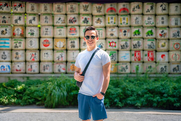 A young happy Latino man smiling in front of decorative sake barrels at Meiji Shrine in Tokyo, Japan, looking happy.