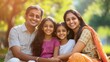 © kitipol - High-resolution photorealistic image of a happy Indian family of four sitting closely together in a sunny park, smiling at the camera. The professional color grading and high-end magazine aesthetic,
