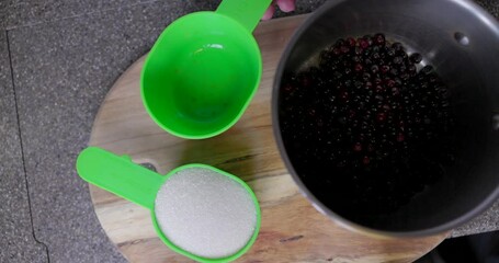 Wall Mural - A green measuring cup with berries and sugar on a wooden cutting board. A silver pot with water next to the berries and sugar