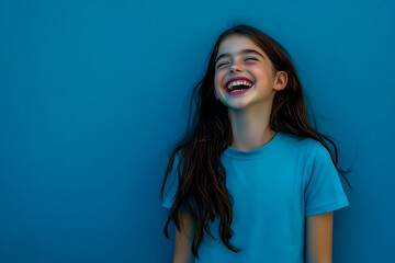 A young girl with long brown hair, laughing and wearing a blue t-shirt.