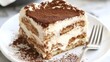 © Pricha.RT - Slice of traditional tiramisu, with creamy mascarpone and cocoa dusting, displayed on a white plate with a fork beside it. The dessert is rich and inviting.
