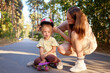 © sementsova321 - Mother putting protective helmet to her daughter before teaching her how to skateboard in the park enjoying outdoor activities for children in summer