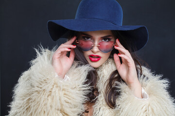 Beautiful fashion model woman in blue classic hat and white fur coat posing indoor, elegance fashion beauty portrait