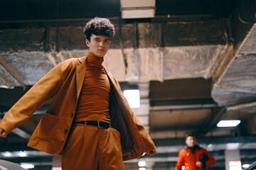 Stylish young man in an orange outfit poses confidently in an underground parking lot