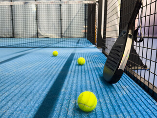 Padel racket and yellow ball behind net on a green court grass turf outdoors at sunset. Paddle is a racquet game. Professional sport concept with space for text