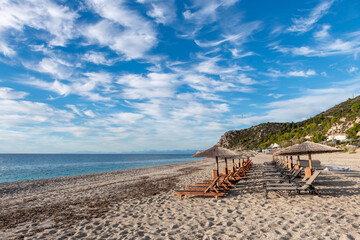 A beautiful sunny afternoon on Kathisma Beach, Lefkada island, Greece, with few visitors, sun beds, blue sea, and sky clouds.