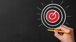 © Apaporn - A hand drawing a target symbol on a black chalkboard with a yellow pencil. Focus on achieving goals and success in business.